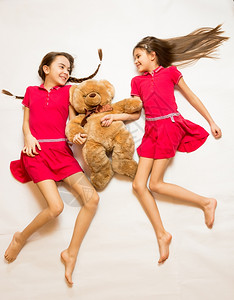 拍摄两名微笑的女孩躺在地板上抱着泰迪熊图片