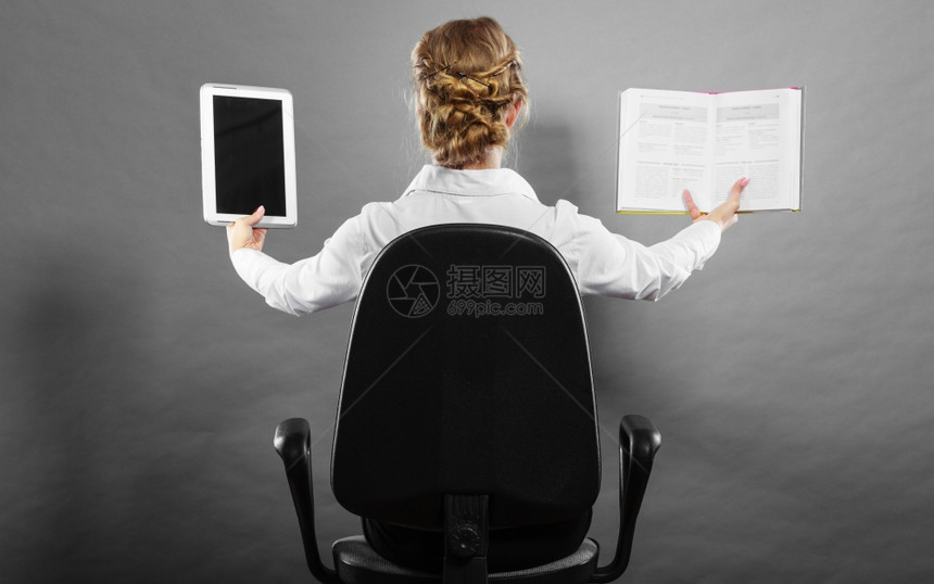 Ebookvsbook坐在椅子上持有传统书籍和电子阅读器平板电脑的女士背对视图粗景图片