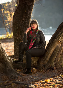 美丽的黑发女坐在秋天公园的大树下背景图片