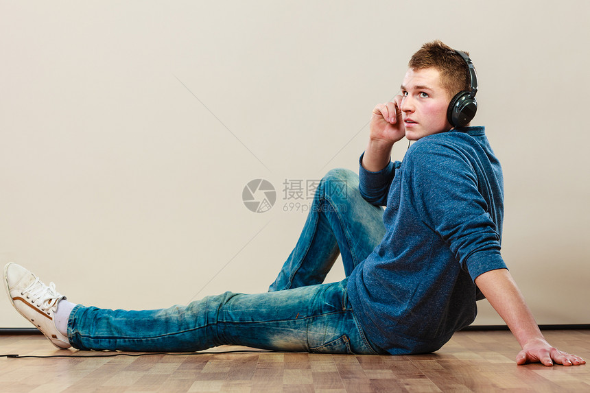 年轻时装男耳机坐在地板上听音乐图片