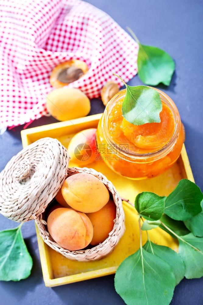 新鲜的杏子和果酱放在桌边的玻璃库里图片