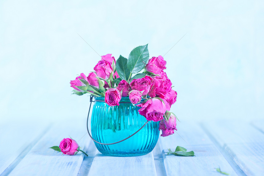 一群小粉红玫瑰花瓶在木制桌子上的玻璃花瓶里图片