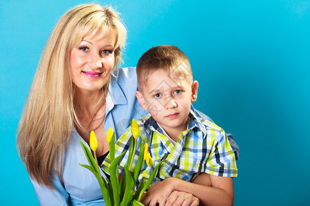 男孩庆祝母亲39日男孩庆祝母亲39日小孩子男给妈工作室送黄色的郁金香花给妈拍蓝色背景图片