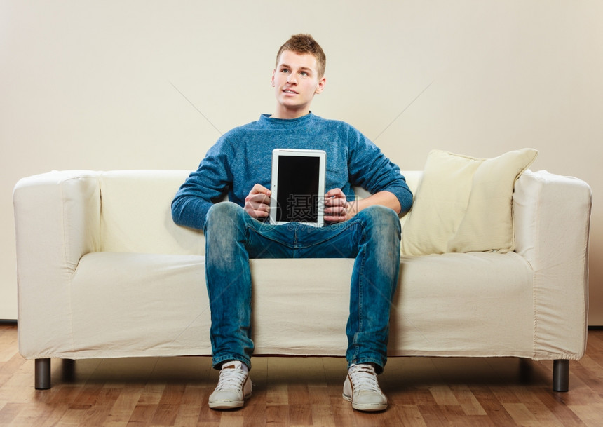 坐在沙发上屏幕显示空白复制间的青少年男在沙发上坐着计算机平板电脑在屏幕上显示空白复制间图片