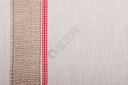 天然亚麻背景的鲜亮织物纺品材料上的黄麻网和红丝带背景图片