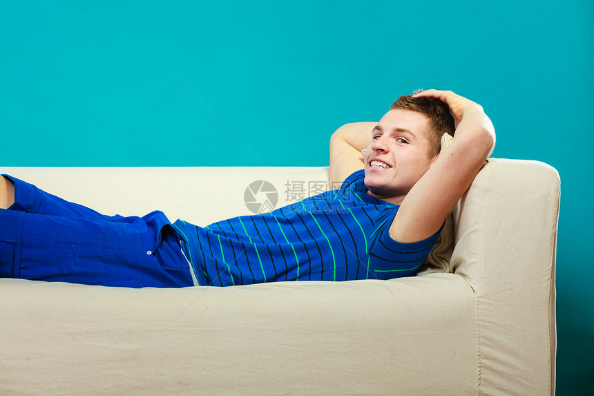 年轻男人在沙发上放松年轻男孩躺在床上懒蓝背景图片