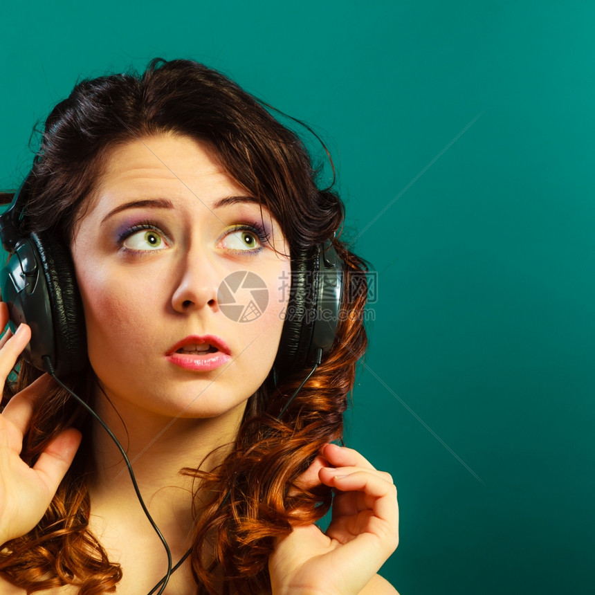 在大耳机里关紧的年轻可爱女孩听音乐放松绿色蓝背景图片
