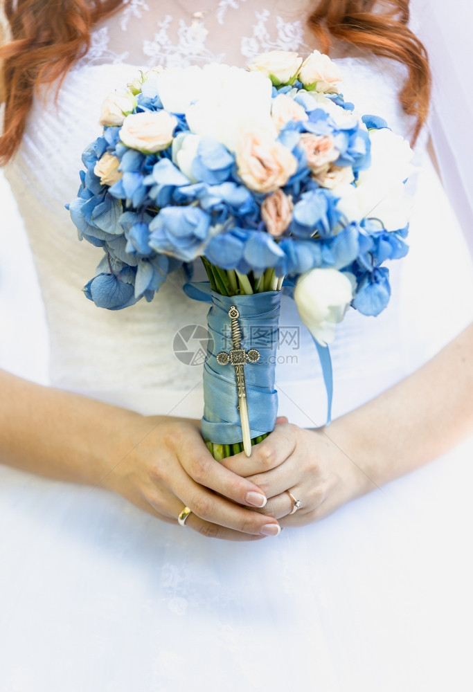 美的年轻新娘拿着蓝色鲜花的新娘束图片