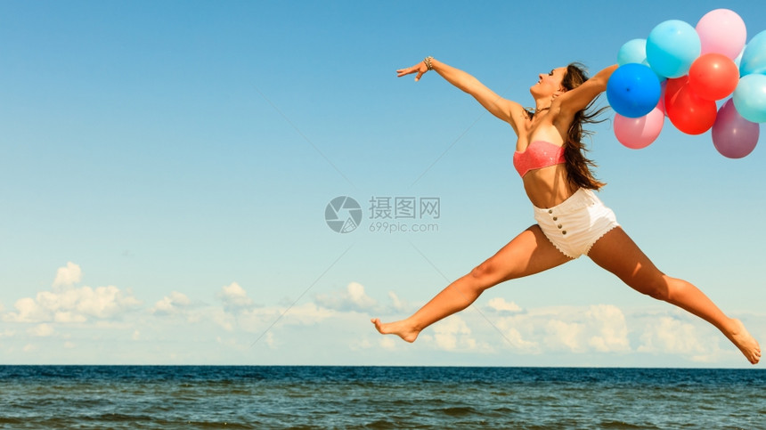暑假庆祝活动和生方式概念阳光明日媚的海滩上有吸引力的运动女少在海滩外用彩色气球跳跃图片