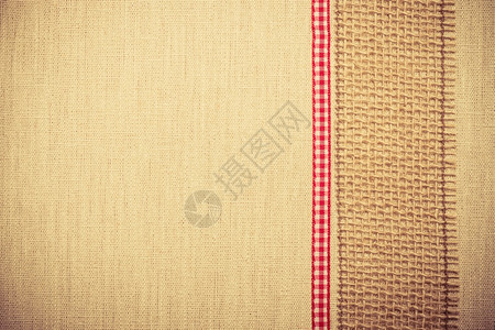 天然亚麻背景的鲜亮织物纺品材料上的黄麻网和红丝带图片