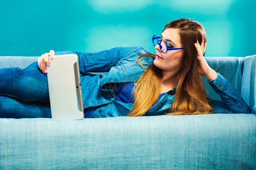 现代技术休闲和年轻人概念时装妇女穿着牛仔裤平板坐在沙发上的蓝色图片