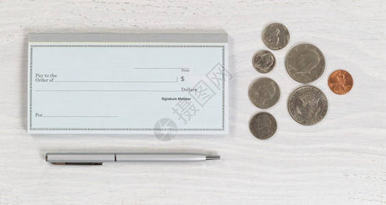白色木制桌面上的空白支票簿银笔和硬币水平版式布局图片