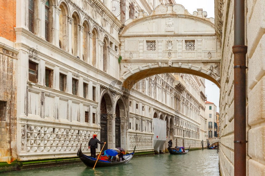 在意大利威尼斯的雨天气下传统歌多拉斯骑在河桥下横滨狭窄的运河上叹气图片