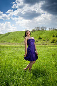 穿紫色裙子的年轻美女在阳光明媚的白天在草地散步图片