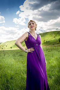 高雅金发美女的肖像穿着长紫色裙子在阳光明媚的白天在草地上摆姿势背景图片