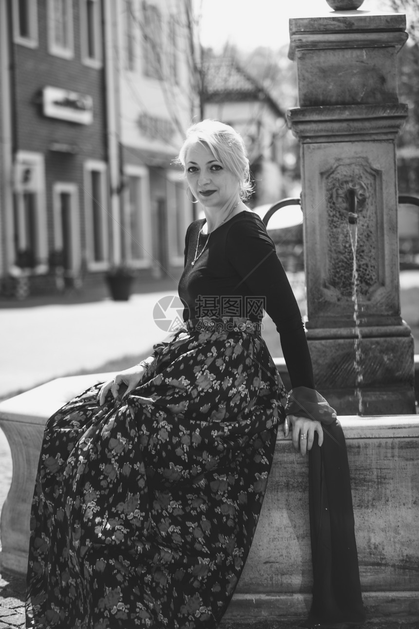 在老街的喷泉里放松穿着长裙优雅女子黑白肖像图片