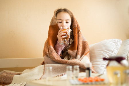 穿着毯子喝热茶的可爱生病女孩肖像图片