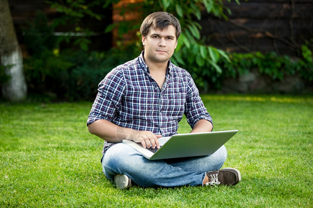 坐在公园草地和笔记本电脑打字的年轻笑着微学生图片