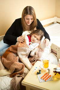 抱着生病女孩躺在床上的年轻有照护母亲的肖像图片