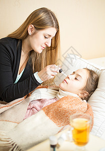 母亲给躺在床上生病的女儿提供鼻喉药物的肖像高清图片