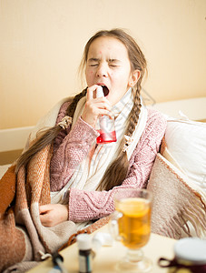 生病的小女孩躺在床上并使用喉咙喷雾剂图片