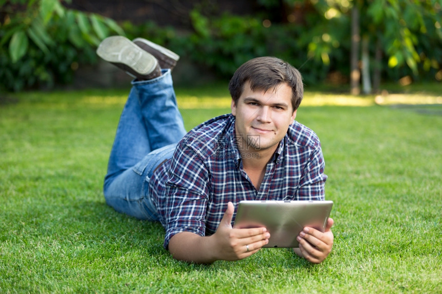 坐在草地上的公园里带着数字平板电脑的帅气笑着微学生图片