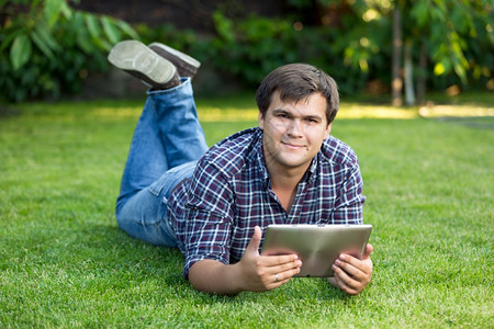 坐在草地上的公园里带着数字平板电脑的帅气笑着微学生图片