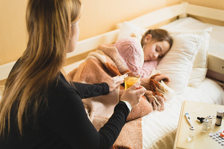 年轻有照顾的母亲给躺在床上的女儿喝热茶图片