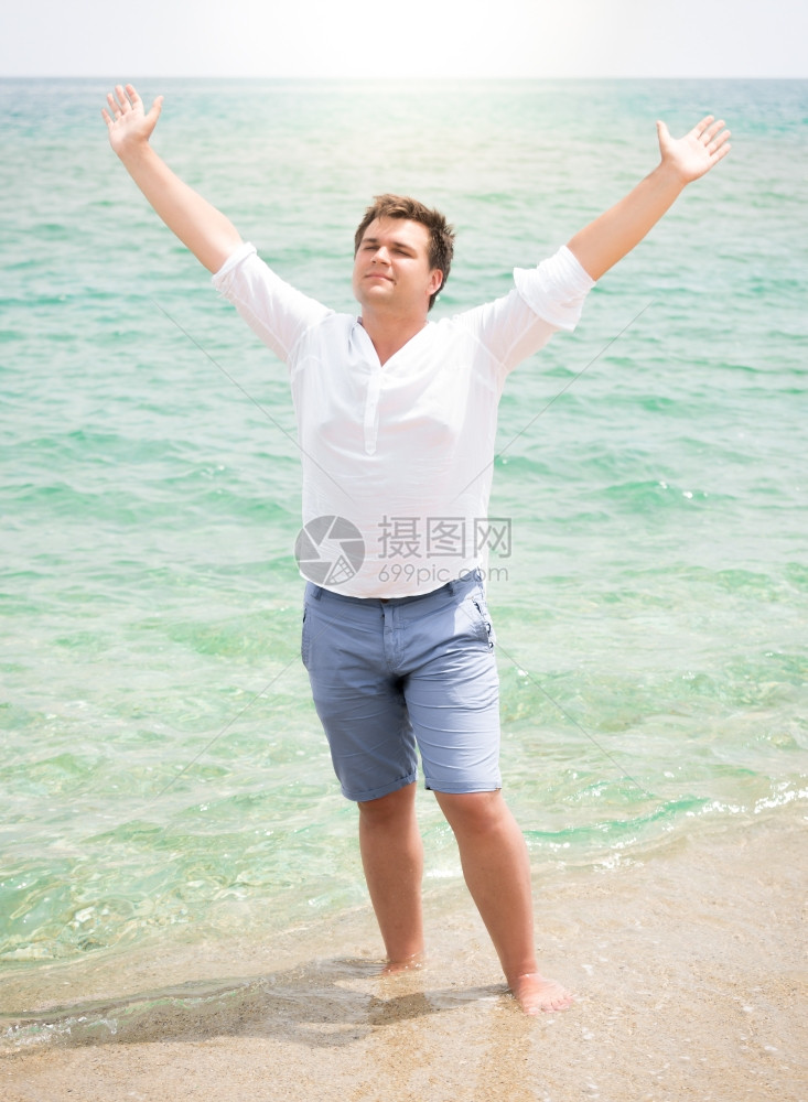 穿白衬衫的帅哥享受海洋举起手在天空中来图片