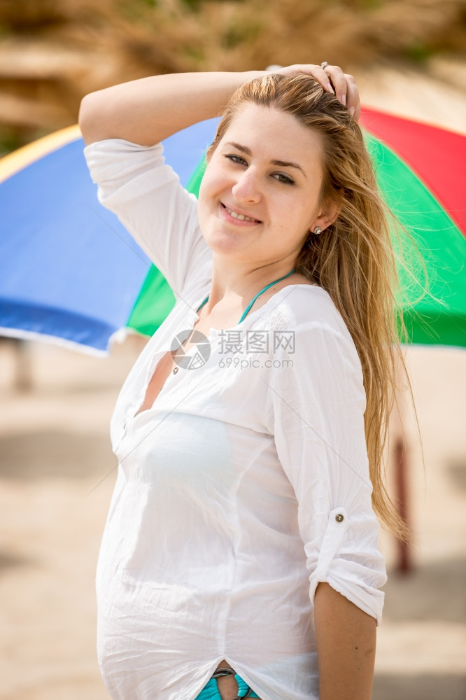 穿着白衬衫的可爱女人肖像假扮在海滩上与太阳雨伞对抗图片