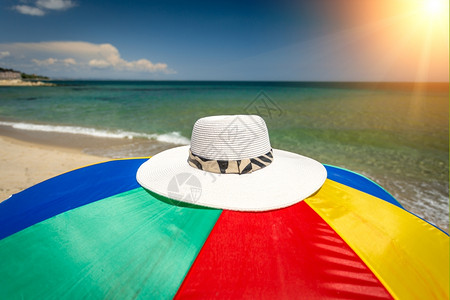 坐在海滨多彩雨伞上的帽子概念镜头图片