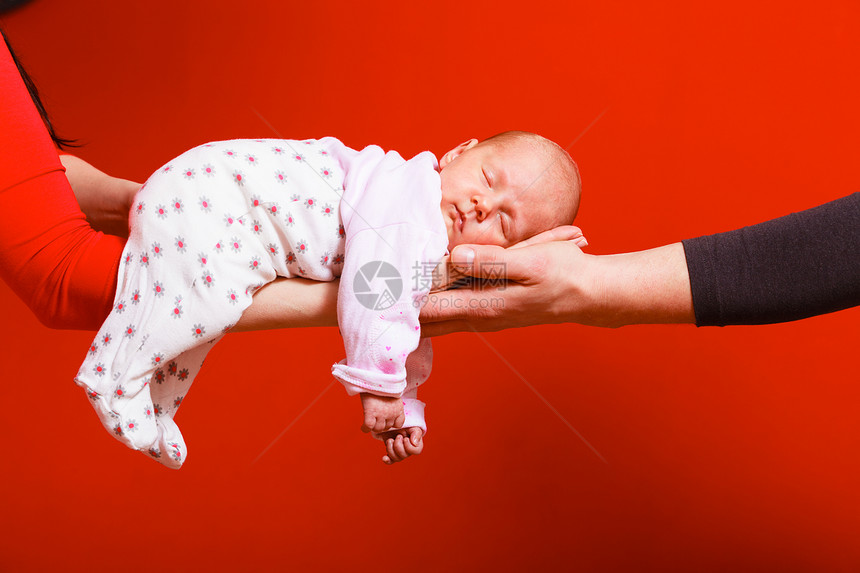 一个月大的女婴睡在父母怀抱红色背景的舒适中图片