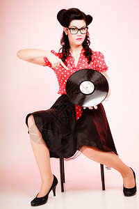 Retro全年时髦的穿眼镜女指着粉红色的旧黑乙烯胶唱片背景图片