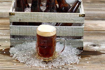 冰霜玻璃杯黑色啤酒集中在前面旧箱装满瓶啤酒碎冰在生锈木板上图片
