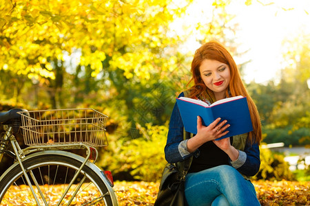 秋天的生活方式概念红发年轻女孩在秋天公园读书中放松独自坐在长椅上图片