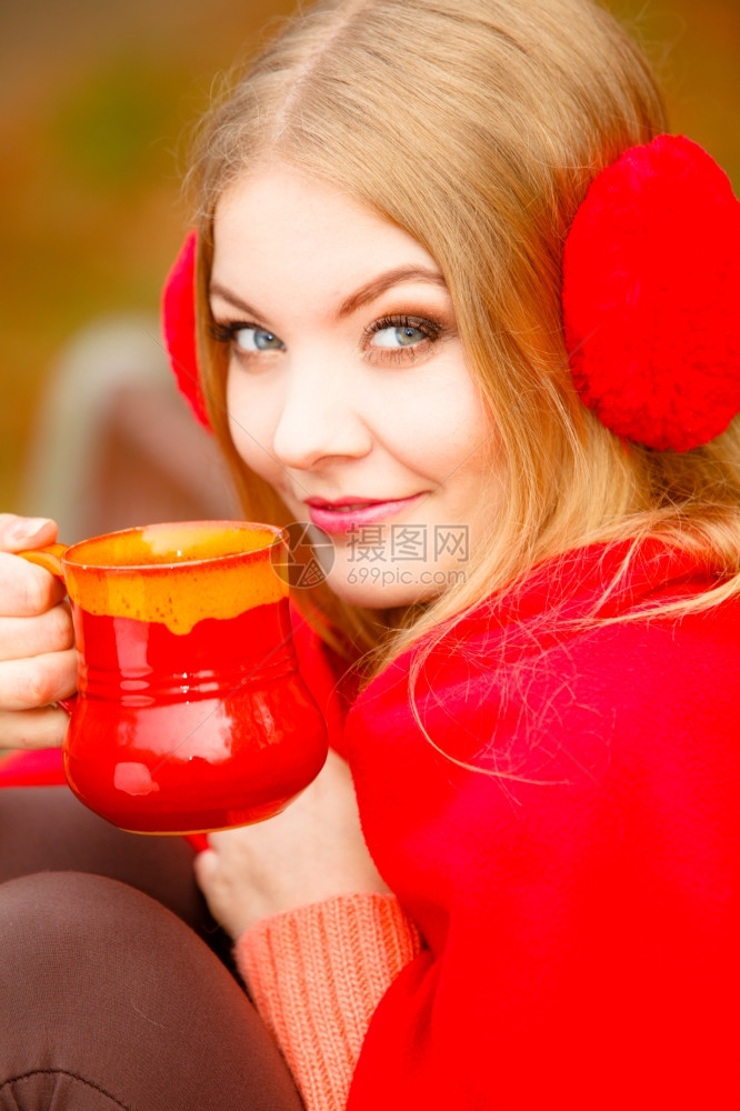 快乐的年轻女子在秋天公园享受热饮喝着红杯热饮橙叶背景图片