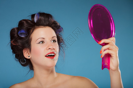 年轻女子准备参加派对玩得开心女孩发型卷的看着镜子倒影风格蓝色背景图片