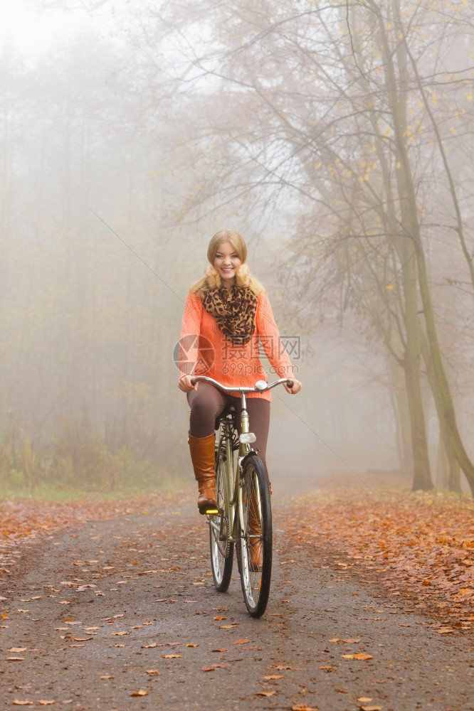 穿着套头毛衣的女人在森林里骑着自行车图片