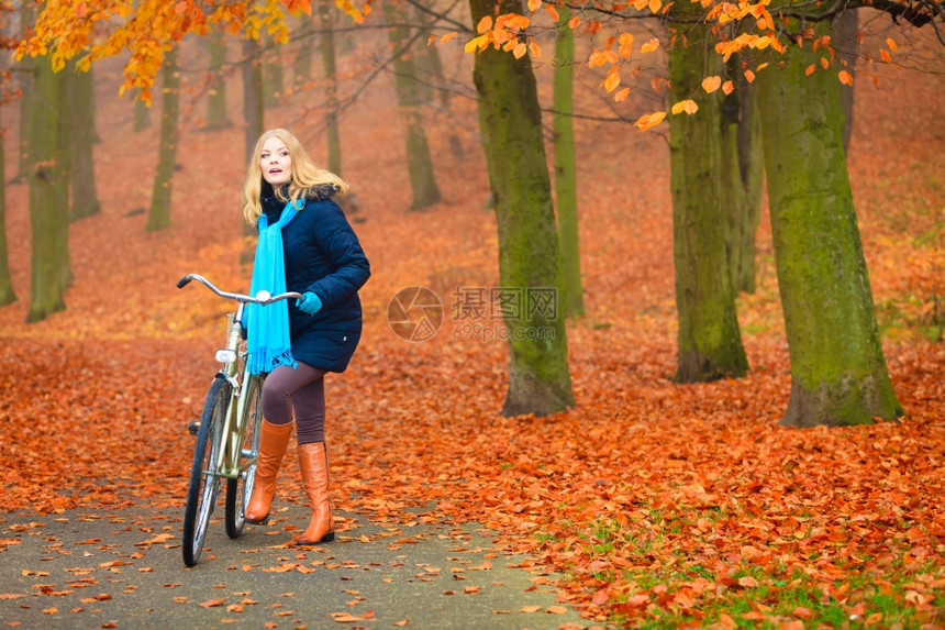 穿着夹克和围巾的女子在户外森林骑自行车图片