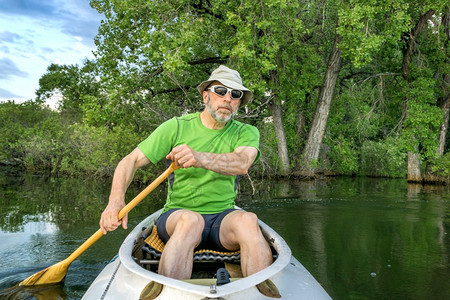 穿着甲板探险独木舟的高级男护板在一片平静的湖边树木背景之下图片