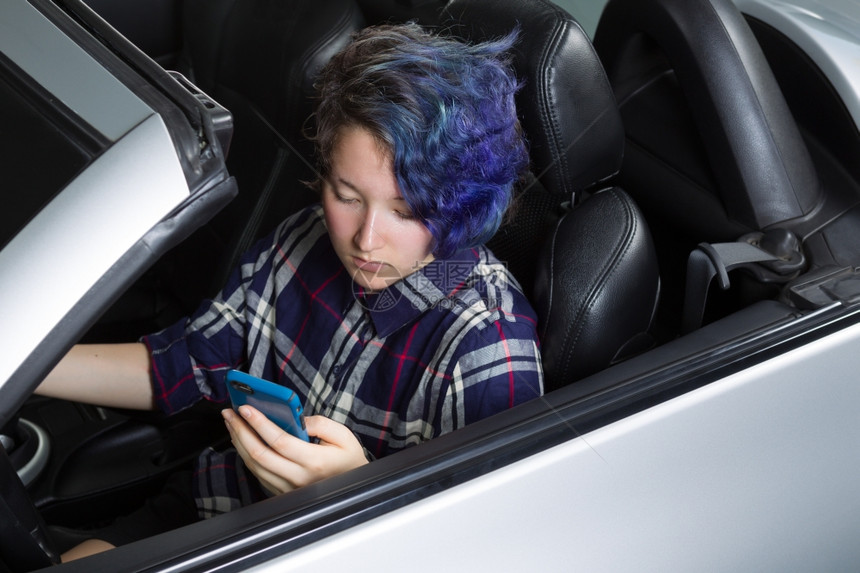 年轻女孩在汽车驾驶座上发短信时低头看手机专注脸部亚洲和高加索混合女孩图片