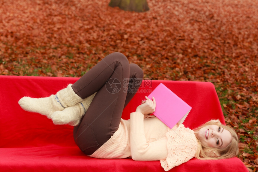 快乐的微笑女子在秋天公园与书一起放松年轻的金发女孩躺在长椅上秋天的生活方式很有趣图片