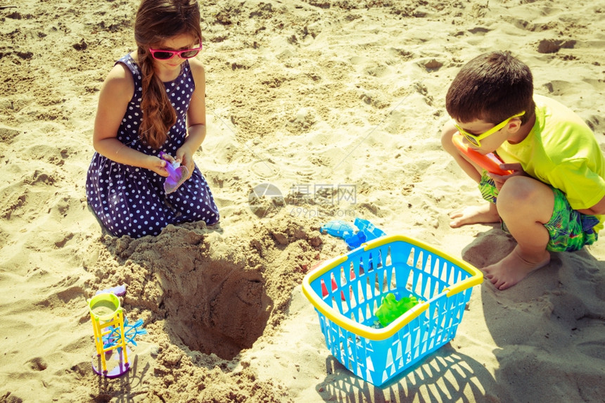 带铲子的小女孩和男儿在沙滩上玩得开心图片