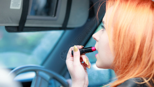 注意力分散年轻女司机红发少在驾驶汽车时涂唇膏补妆背景