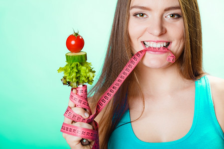 健美和减肥概念合适的女人用新鲜蔬菜咬胶带工作室拍摄绿色背景图片