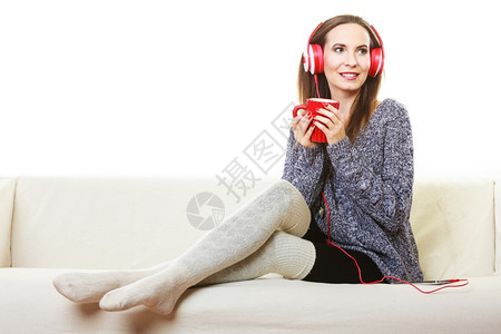 妇女随便的红色大耳机听音乐mp3坐在沙发上家休息喝热茶背景图片