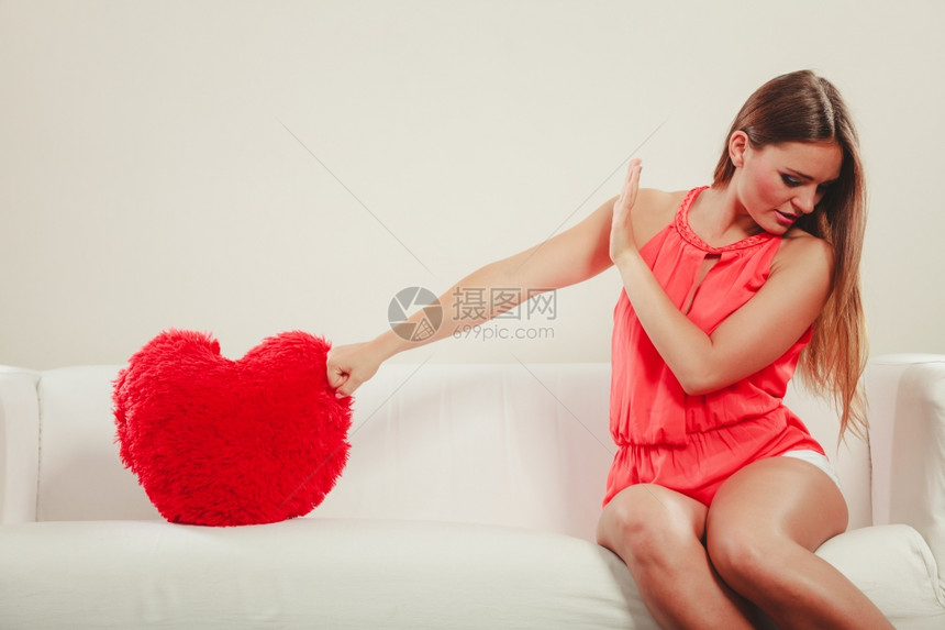 悲伤的年轻女孩红心的枕头坐在白沙发上情人节的爱图片