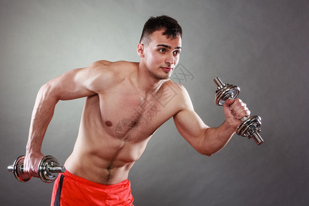 健壮体强的人与哑铃一起锻炼运动近身肌肉的年轻人举起重量的黑暗背景图片