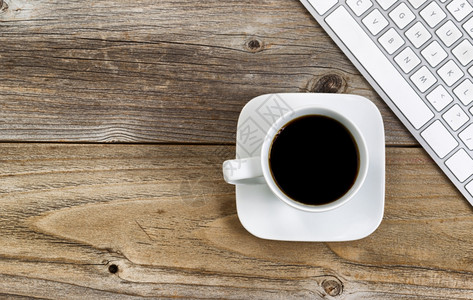 黑咖啡的顶端选择地关注咖啡杯的上唇部分电脑键盘在锈木上图片