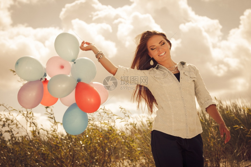 节日庆典和生活方式概念具有吸引力的女模特在云层背景之外持有一连串多彩气球图片
